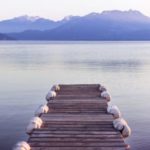 The picture shows a rustic dock leading out into placid water.