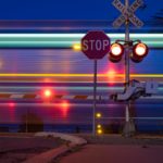 The picture shows a railroad crossing with a train speeding through.