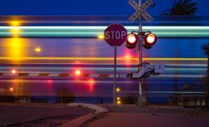 The picture shows a railroad crossing with a train speeding through.