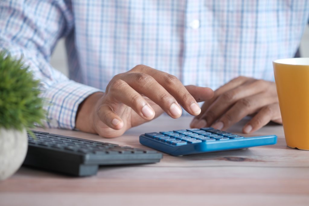 The picture shows the hands of a person using a calculator to represent figuring taxes, donations, and deductions.