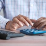 The picture shows the hands of a person using a calculator to represent figuring taxes and deductions.