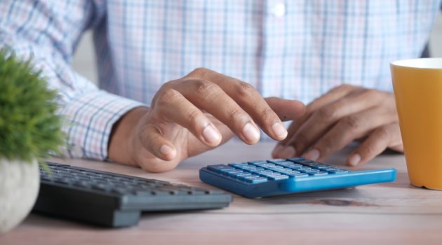 The picture shows the hands of a person using a calculator to represent figuring taxes and deductions.