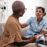 The picture shows an older Black woman talking to her caregiver to represent older adult living.