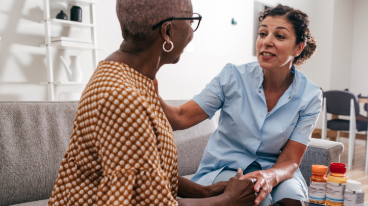 The picture shows an older Black woman talking to her caregiver to represent older adult living.