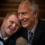 The picture shows a man with Down Syndrome hugging his father happily. ABLE accounts apply to some disabled people.