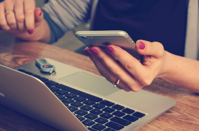 The picture shows a woman looking at her phone and laptop. This represents budgeting software.